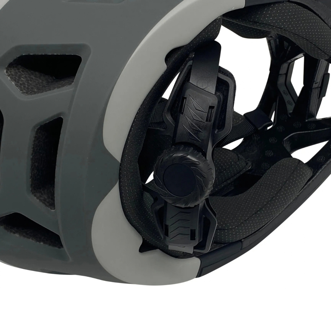 Close-up of a bicycle helmet's rear adjustment system, showing the dark gray shell, white trim, black padding, and dial mechanism against a white background.